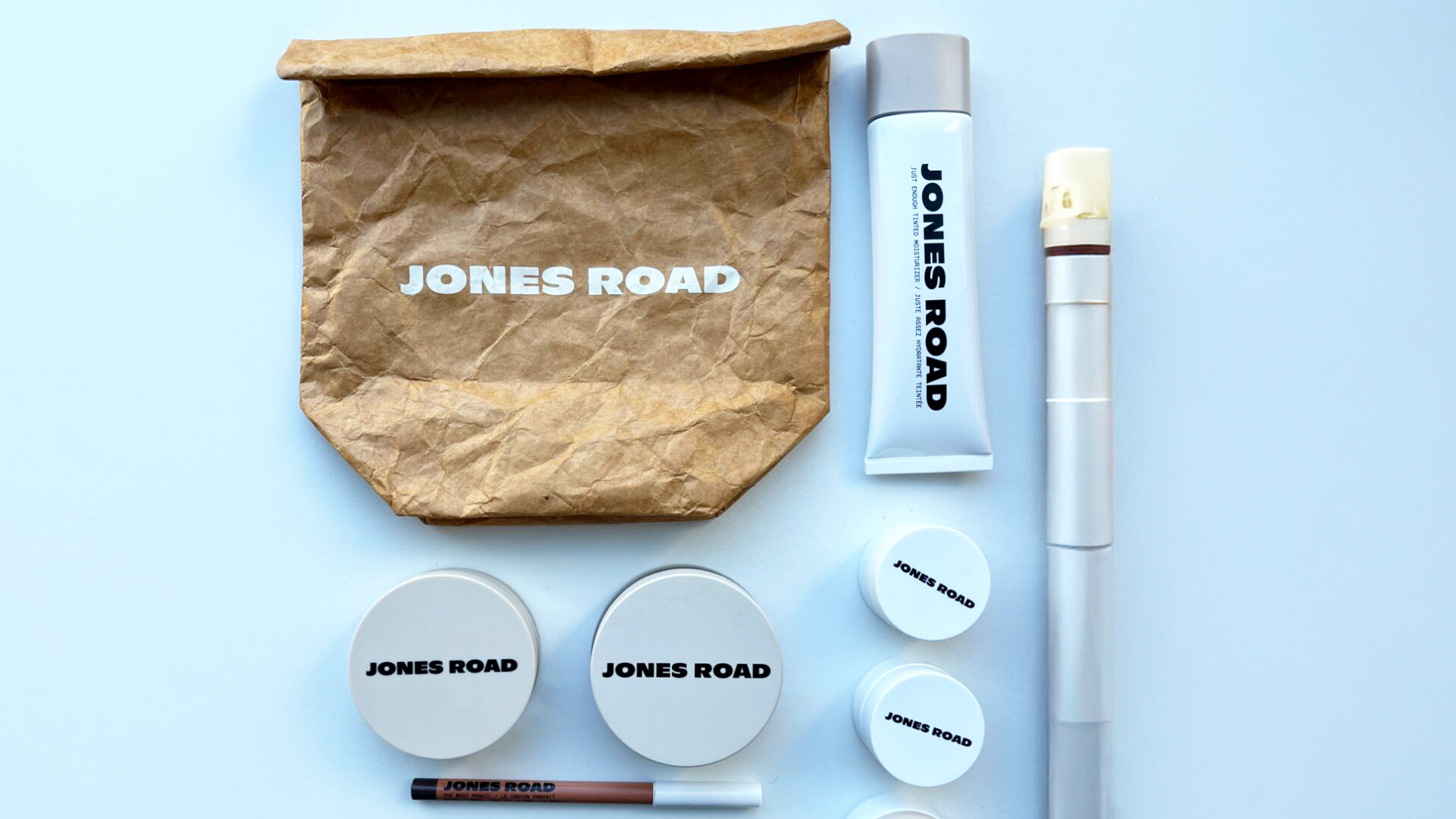 raspakiran paket jones road prodizvoda na stolu, uključujući šminku, puder, olovku...