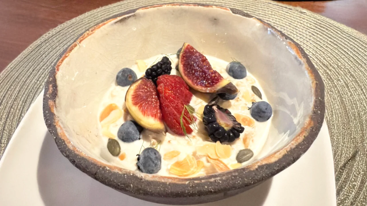 Zdjela s kremastim doručkom od zobenih pahuljica i jogurta, ukrašena smokvama, borovnicama, kupinama i bademima.